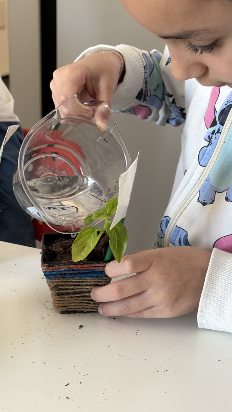 Una bambina annaffia una piantina nel vaso decorato